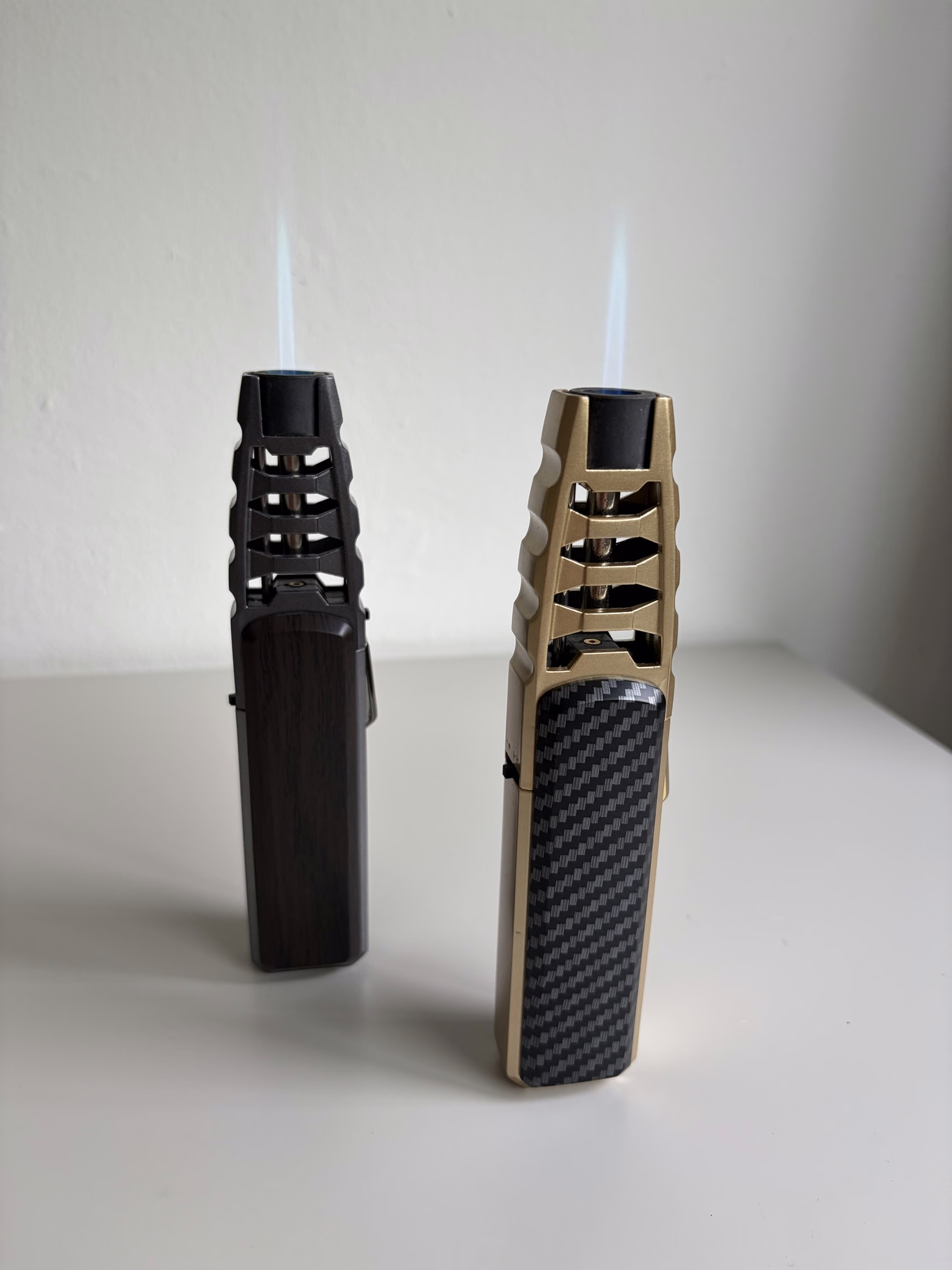 Deux briquets torche debout avec une flamme bleue, à effet bois sombre et finition dorée avec aspect carbone